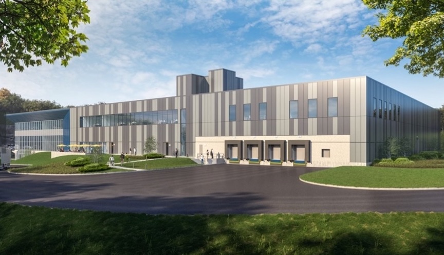 A modern, gray multi-story pharmaceutical facility with loading docks set against a blue sky and green landscape.